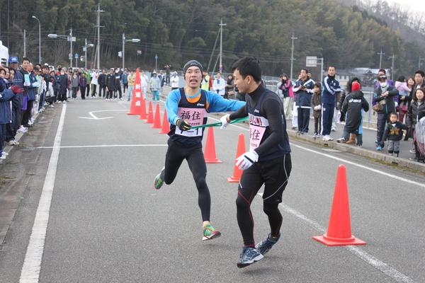 福住と書かれたゼッケンのユニフォームを着た男性が、緑色のたすきを次のランナーに渡している写真